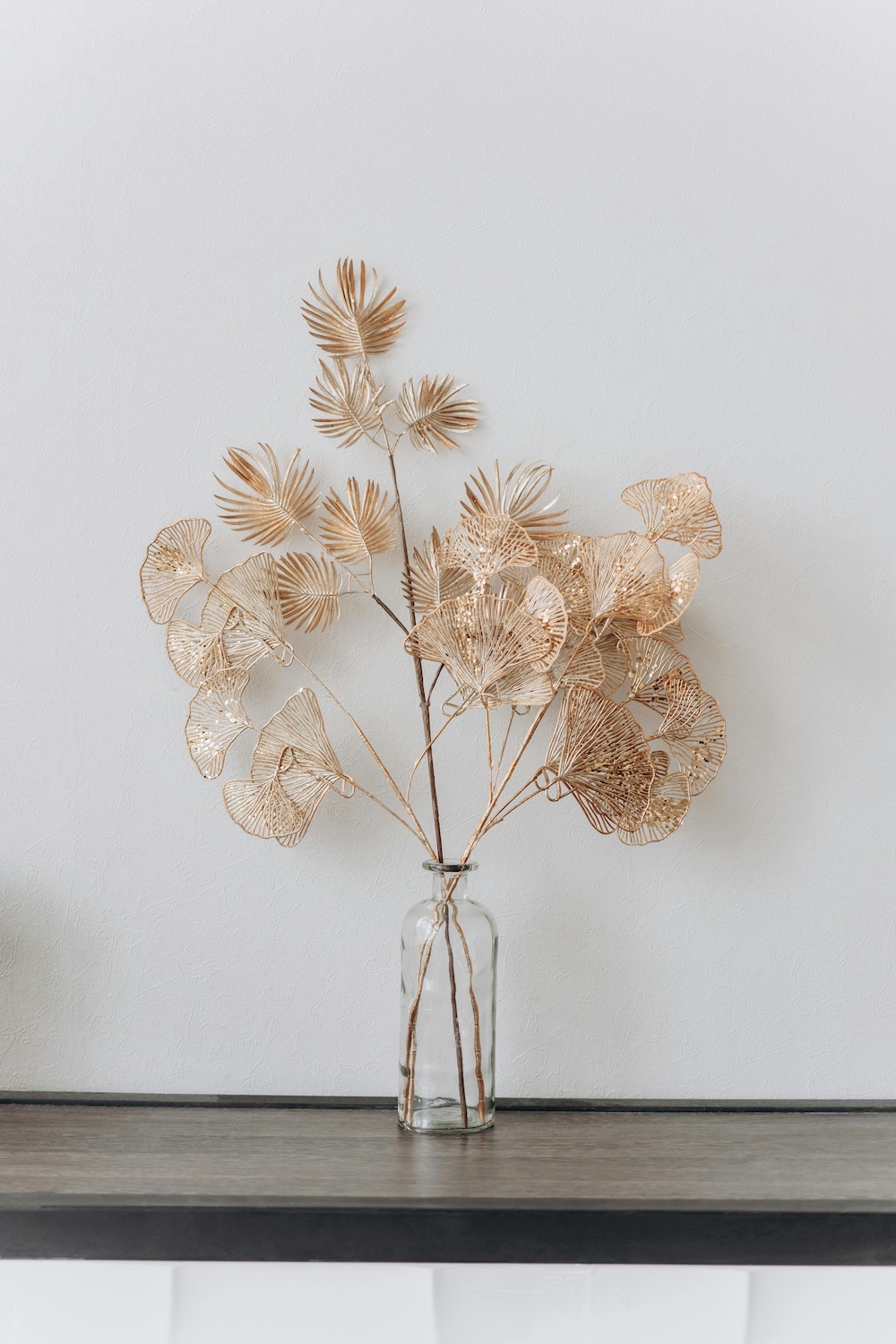 Decorative dried leaves arranged in a glass bottle vase on a wooden shelf